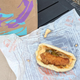 Taco Bell's new Crispy Chicken Sandwich Taco resting on wrapper beside Taco Bell bag